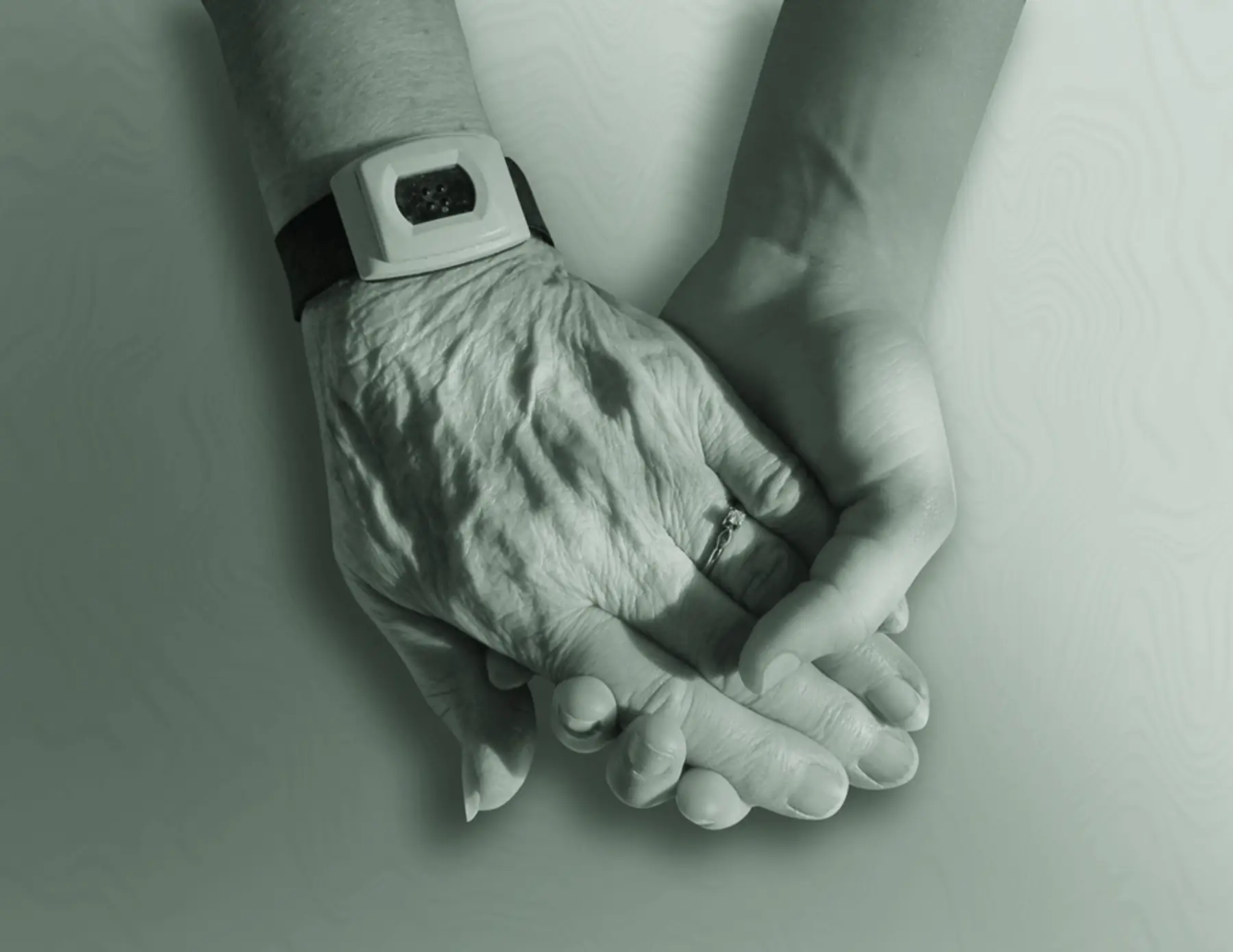 An older person's hand resting in the hands of a supporting carer